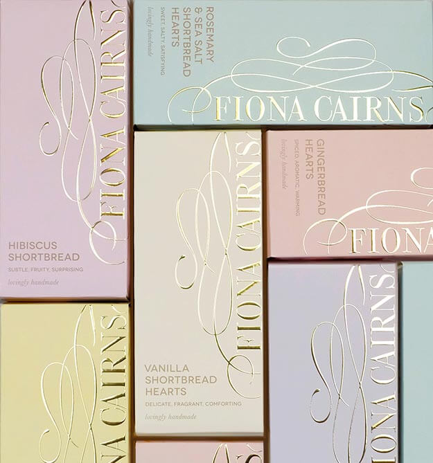 An array of Fiona Cairns Luxury shortbread packaging. Pastel colours. Gold foil logo.