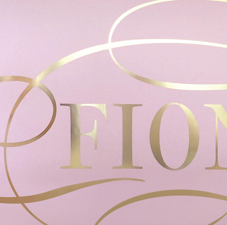 Close up of Fiona Cairns logo on pink background. Gold foil logo. 